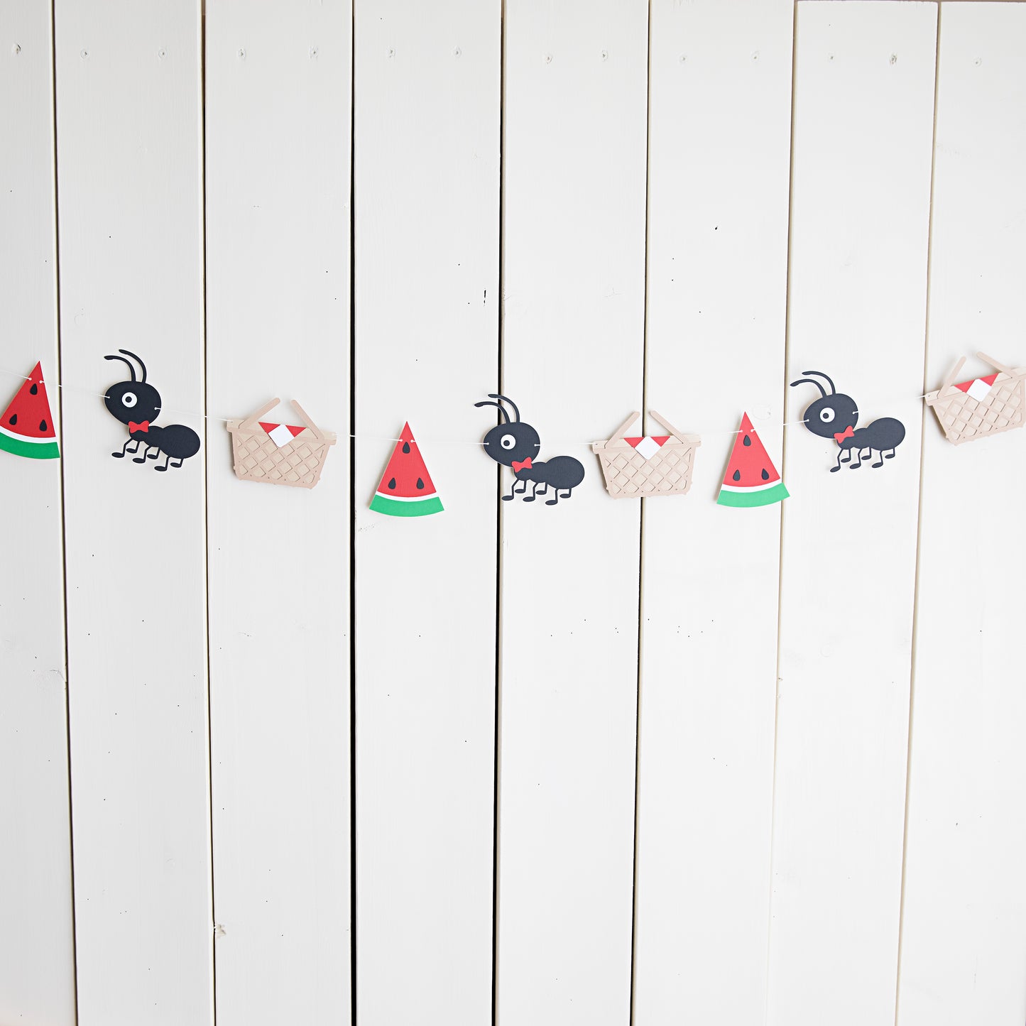 picnic garland featuring ants, picnic baskets, and watermelon strung on twine against a wall