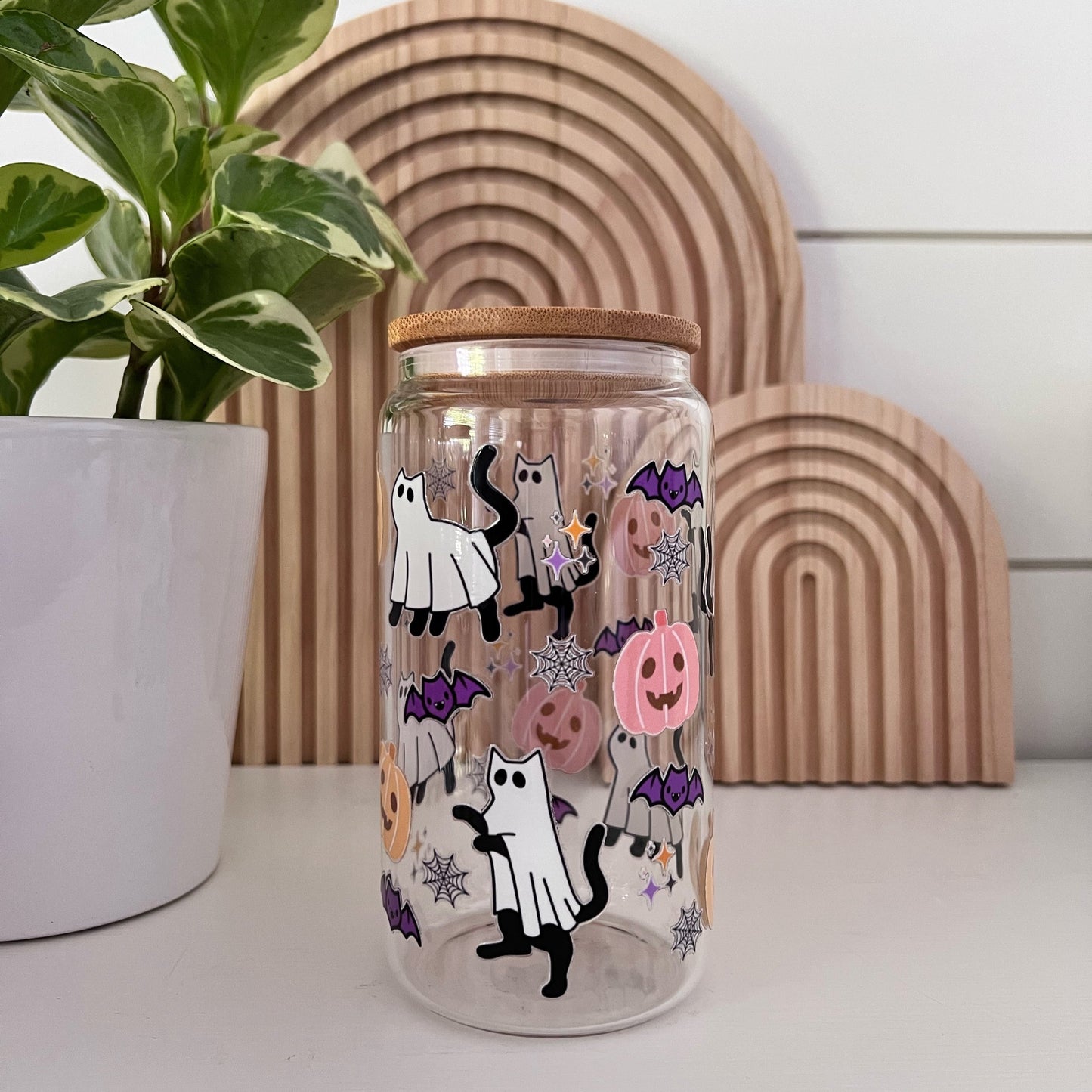 black cats dressed up as ghosts on a glass cup with pastel pumpkins and bat designs
