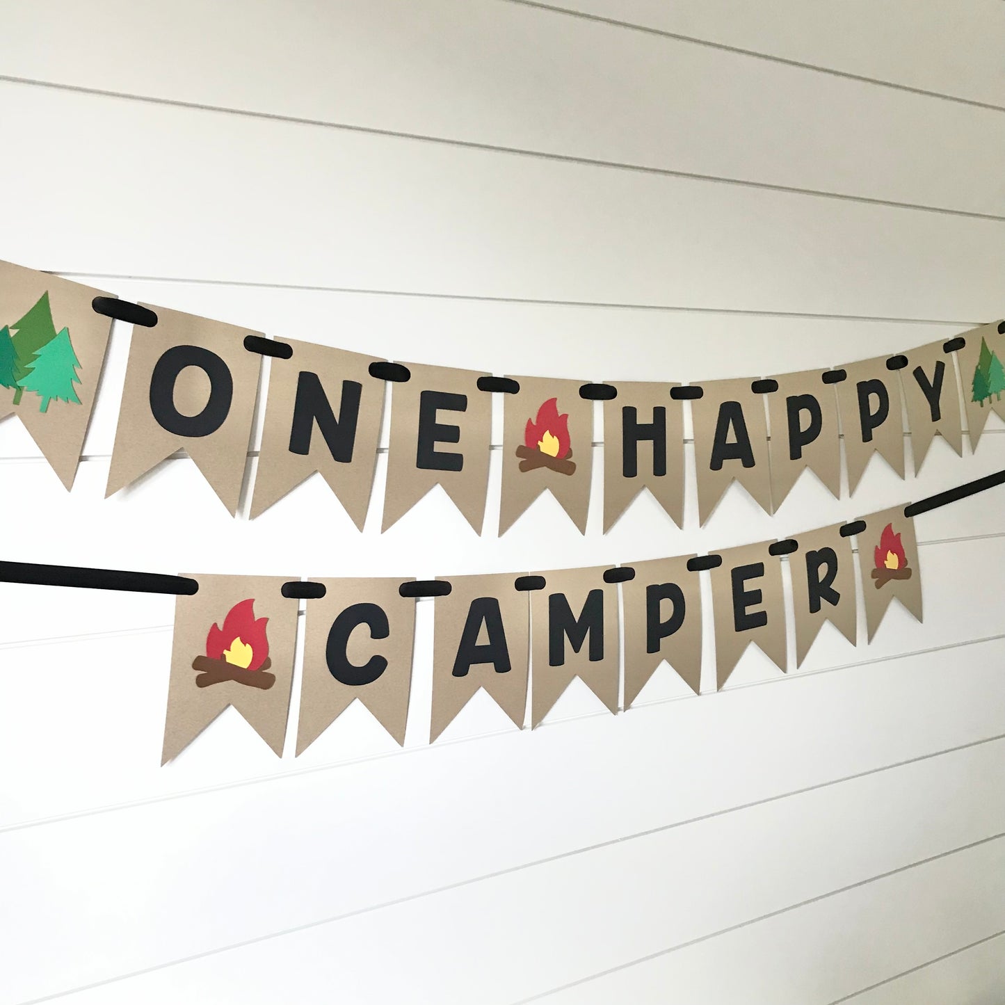 banner in kraft color that says "one happy camper" in black font with tree's and a fire on the ends