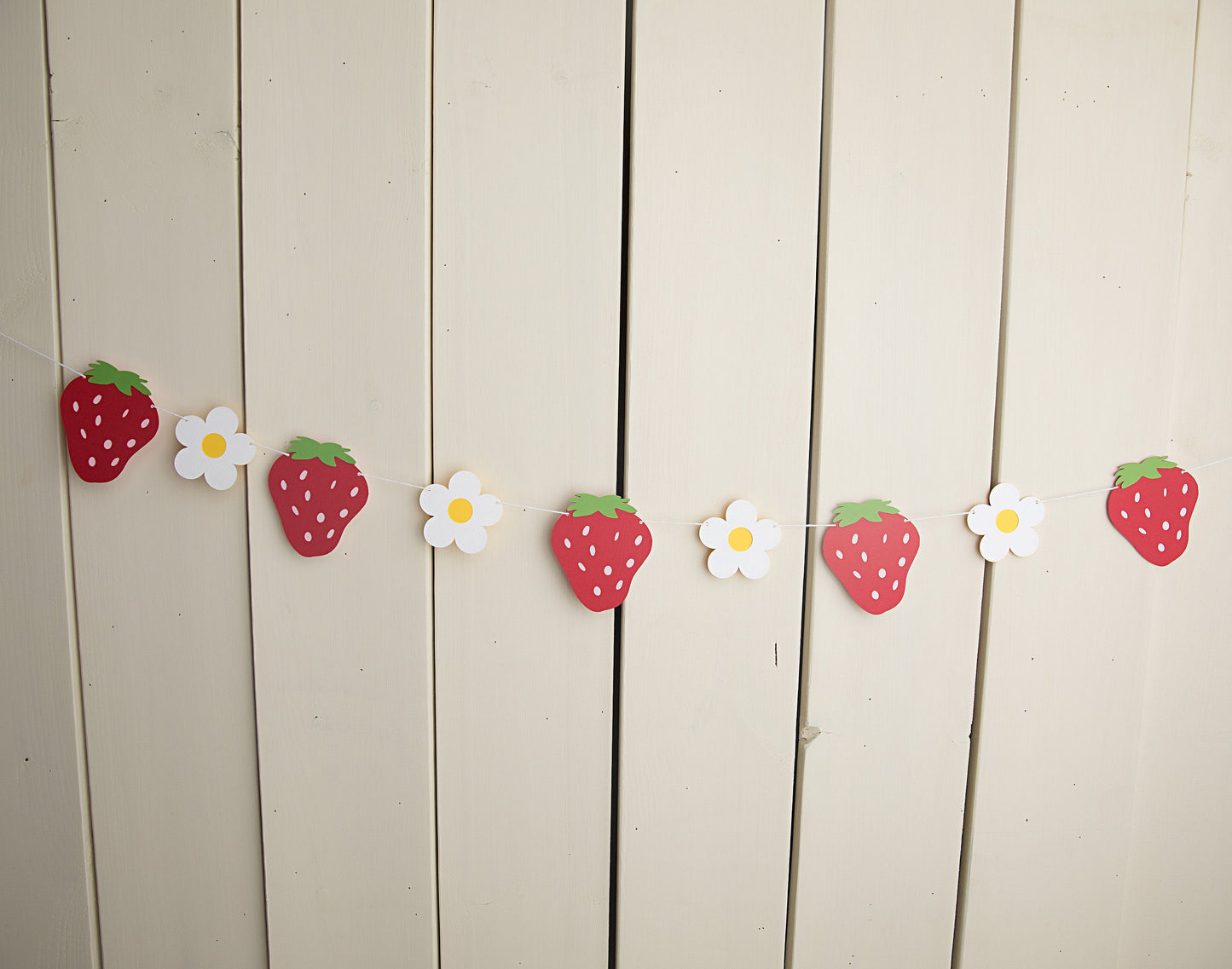 paper strawberries and daisies strung on twine against a wall