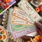 Set of colorful cards with dream harbor book series designs on a wooden table with fall leaves and cookies.