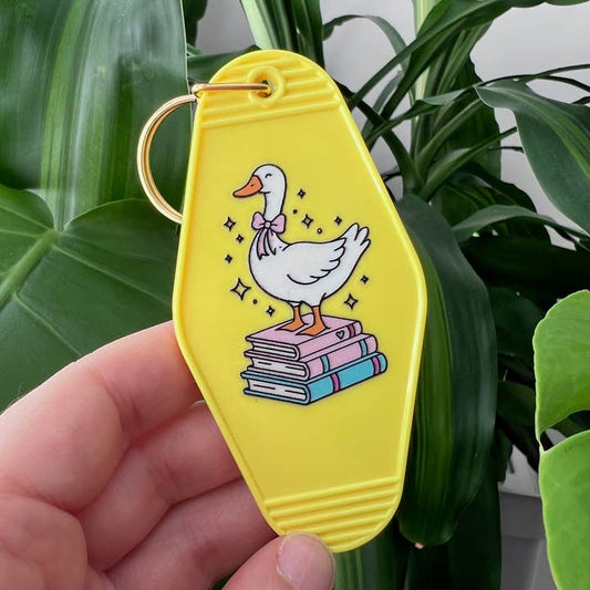 Yellow keychain with a cartoon duck design held in front of green leaves