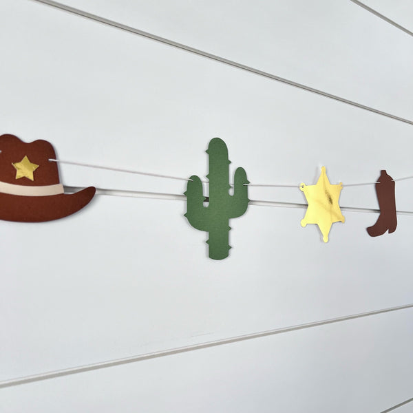 cowboy themed garland with cowboy hats, cacti, gold foil sheriff badge and brown cowboy boots