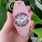 Pink keychain with 'Silly Goose on the Loose Club' design held in a hand with green leaves in the background