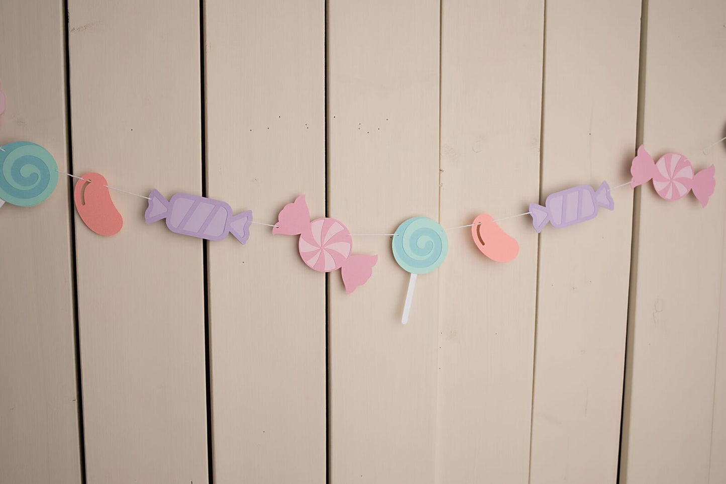assorted pastel candies strung on white twine hanging against wall 