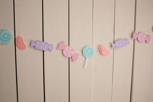 assorted pastel candies strung on white twine hanging against wall 