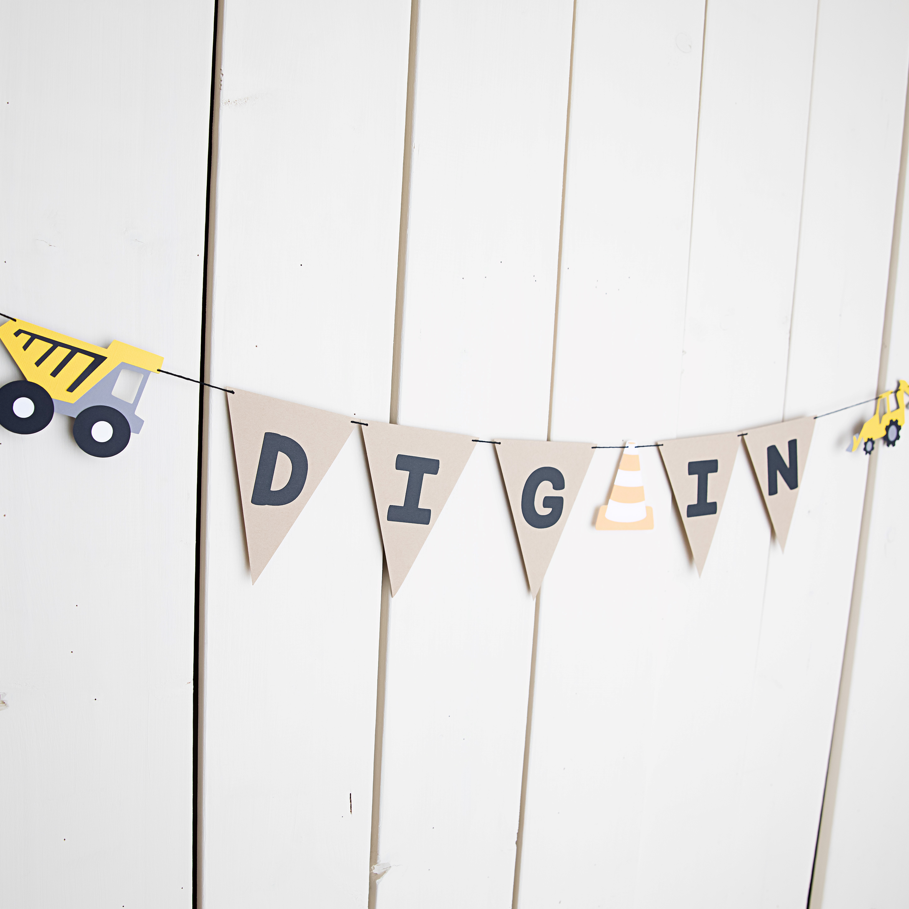 A happy birthday banner with the word 'DIG IN' written on pennants attached to black twine, decorated with construction vehicle figures and placed against a white background.