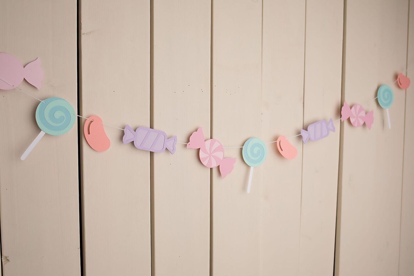 assorted pastel candies strung on white twine hanging against wall 