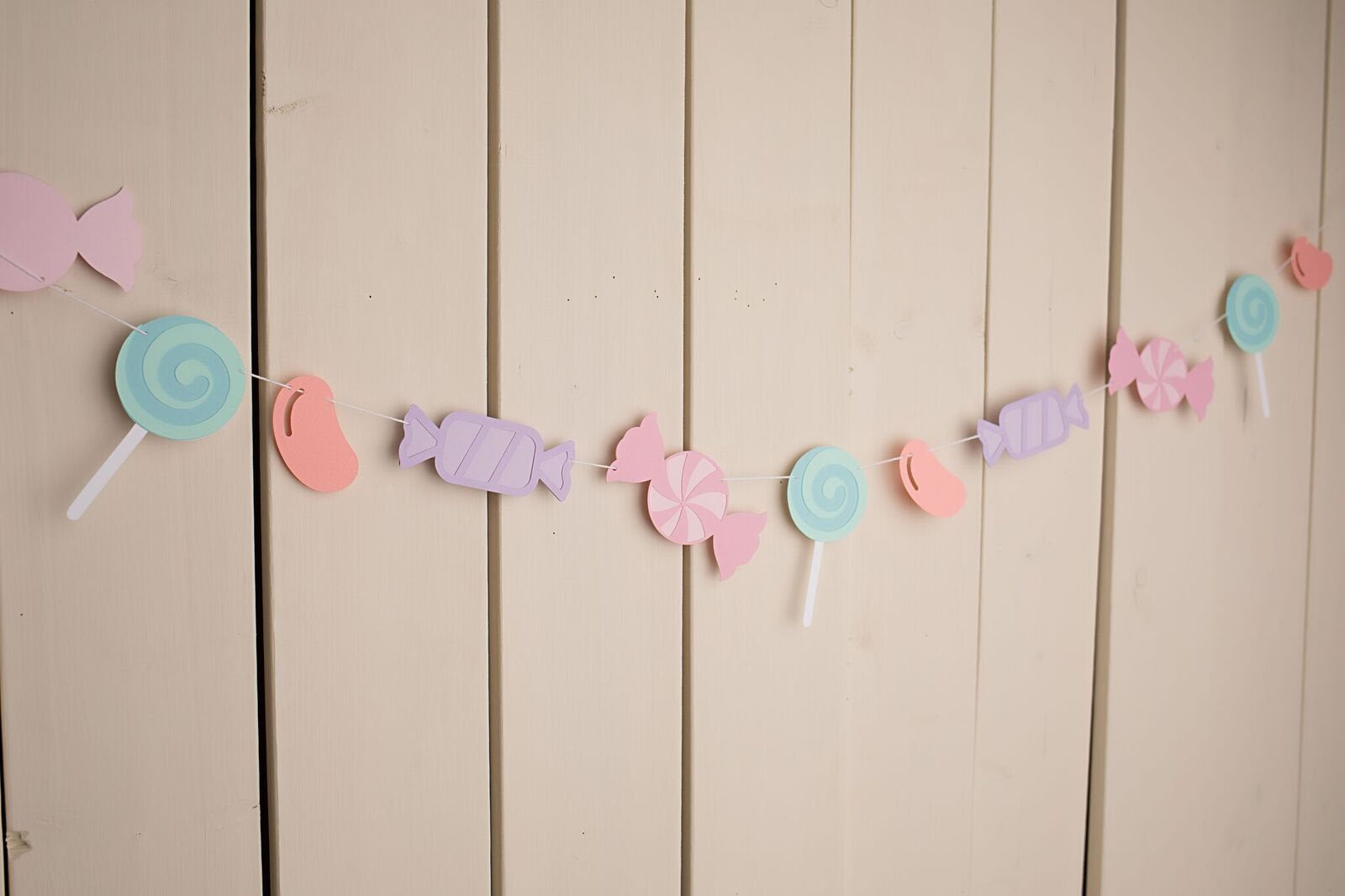 assorted pastel candies strung on white twine hanging against wall 